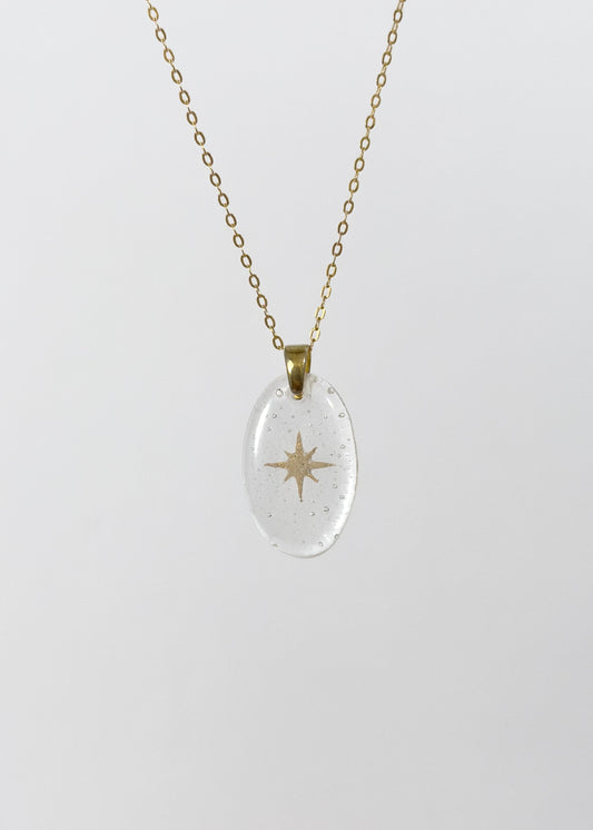 Clear glass pendant necklace with gold star design made out of cremains on a white background
