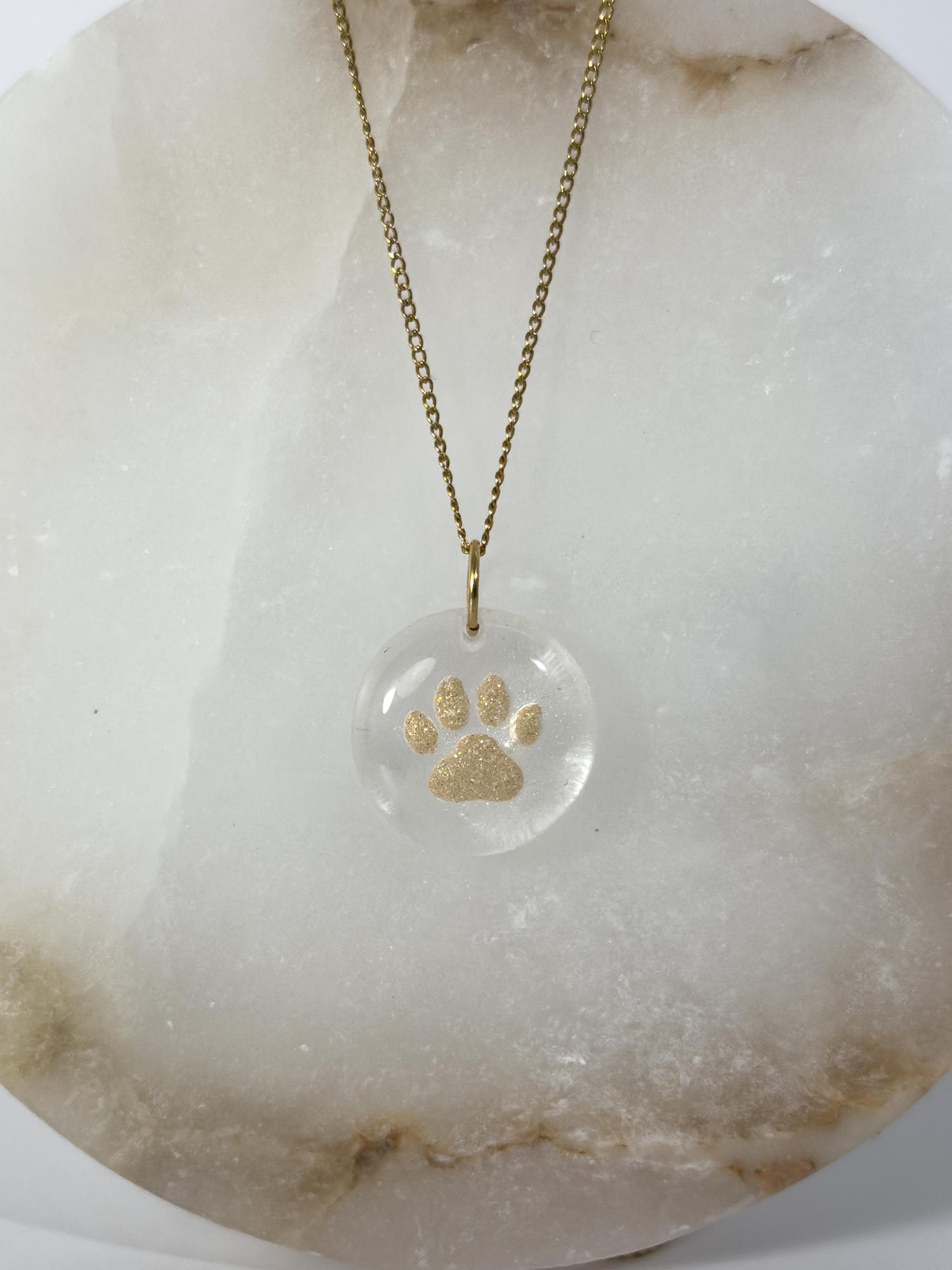 A dog ash memorial necklace where the ashes are mixed with gold mica and shaped into a paw print