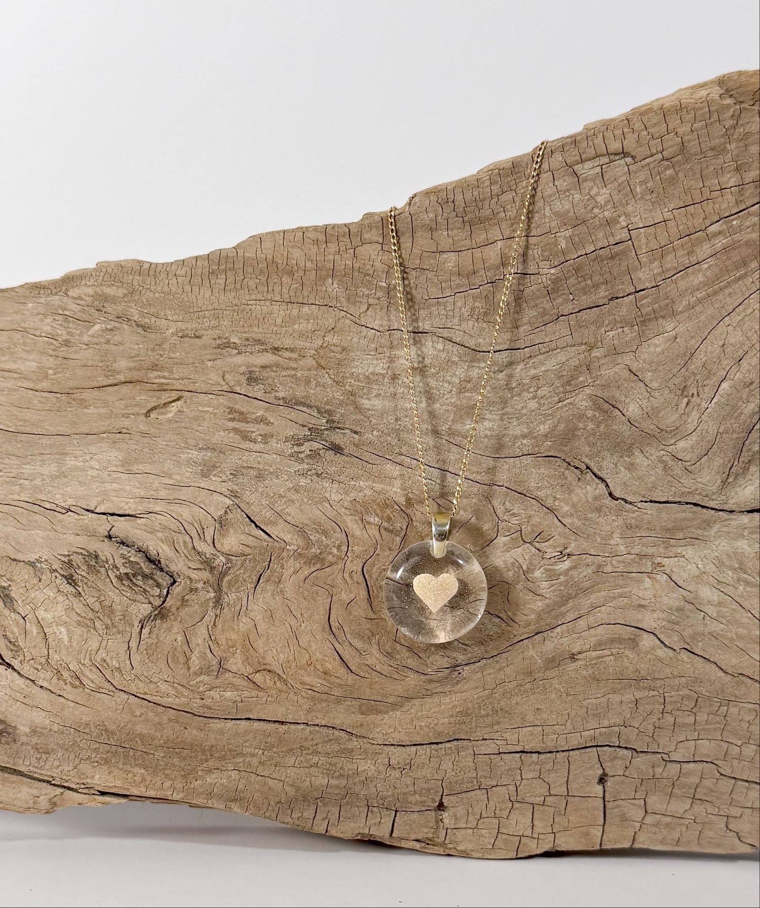 A glass memorial pendant with the ashes and cremains shaped into a heart leaning against a piece of wood.