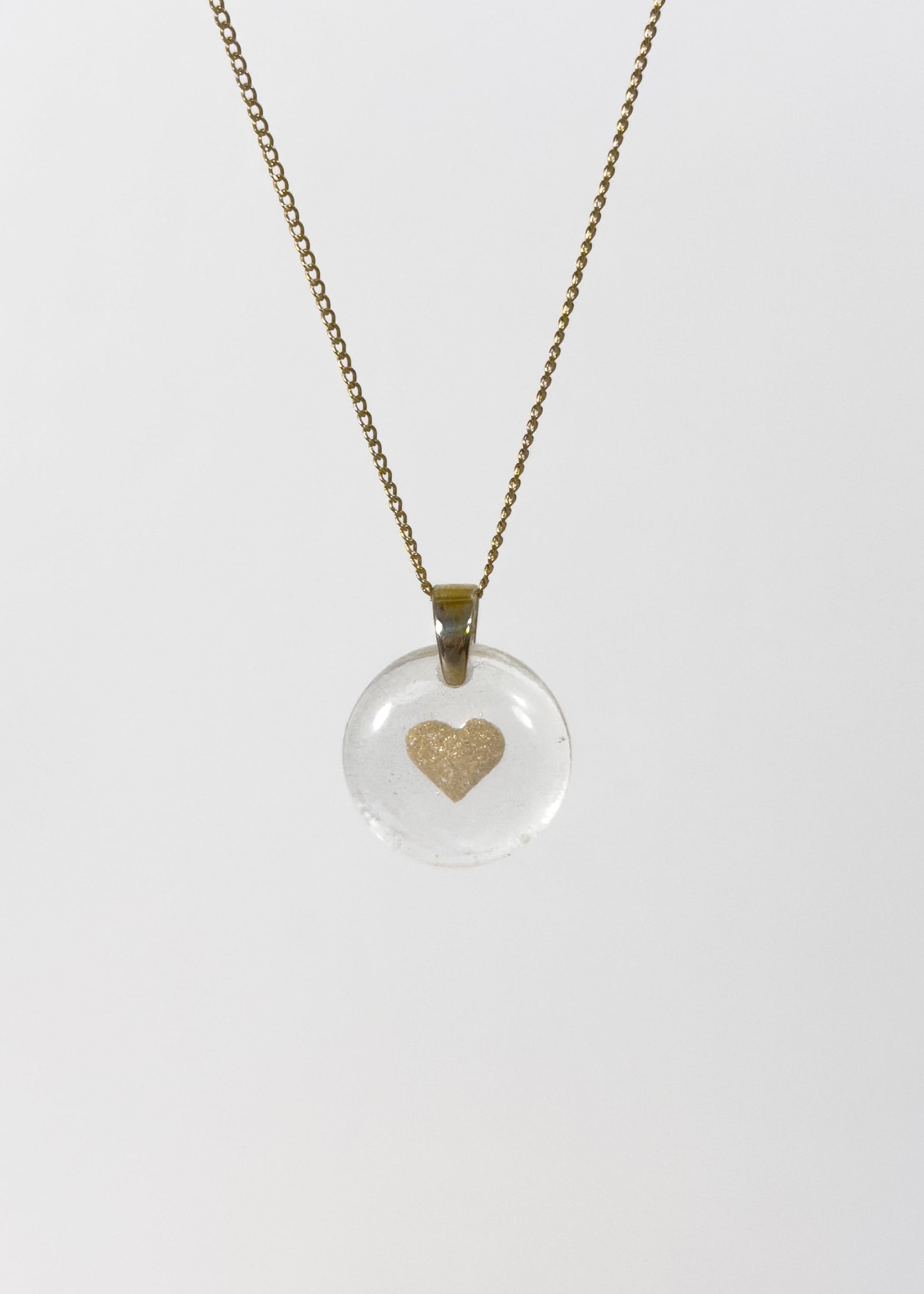 Clear glass pendant necklace with a gold heart design made out of cremains and ashes on a white background