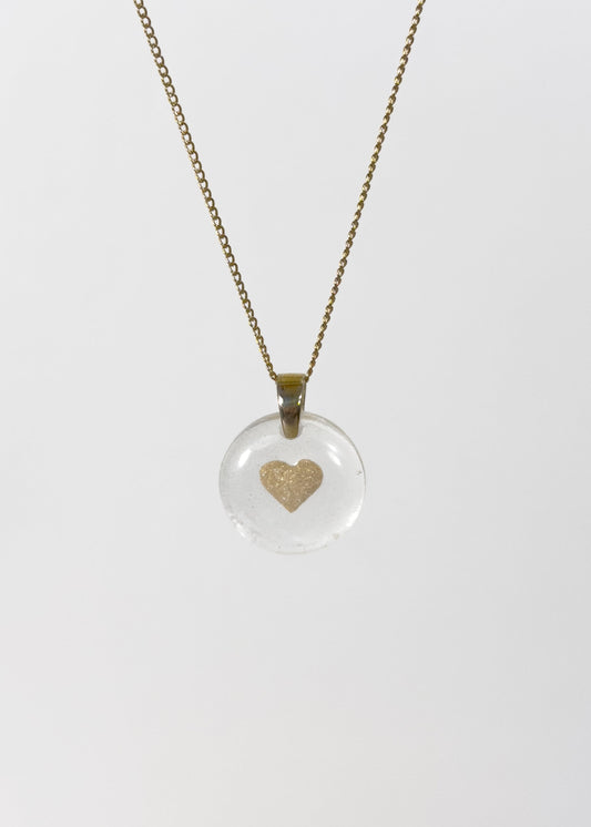 Clear glass pendant necklace with a gold heart design made out of cremains and ashes on a white background