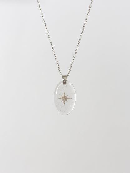 Clear glass pendant necklace with silver star design made out of cremains on a white background