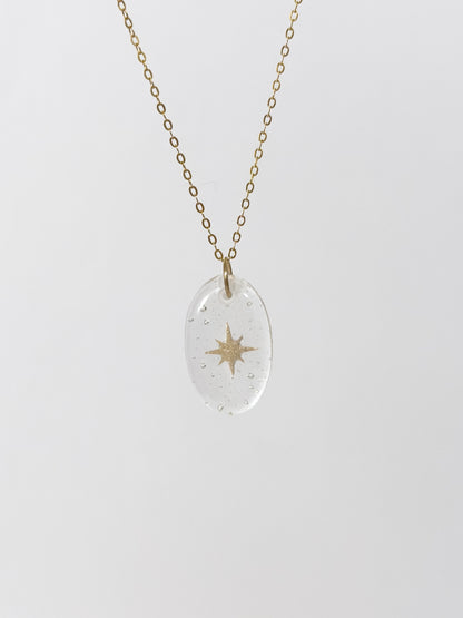 Clear glass pendant necklace with gold star design made out of cremains on a white background