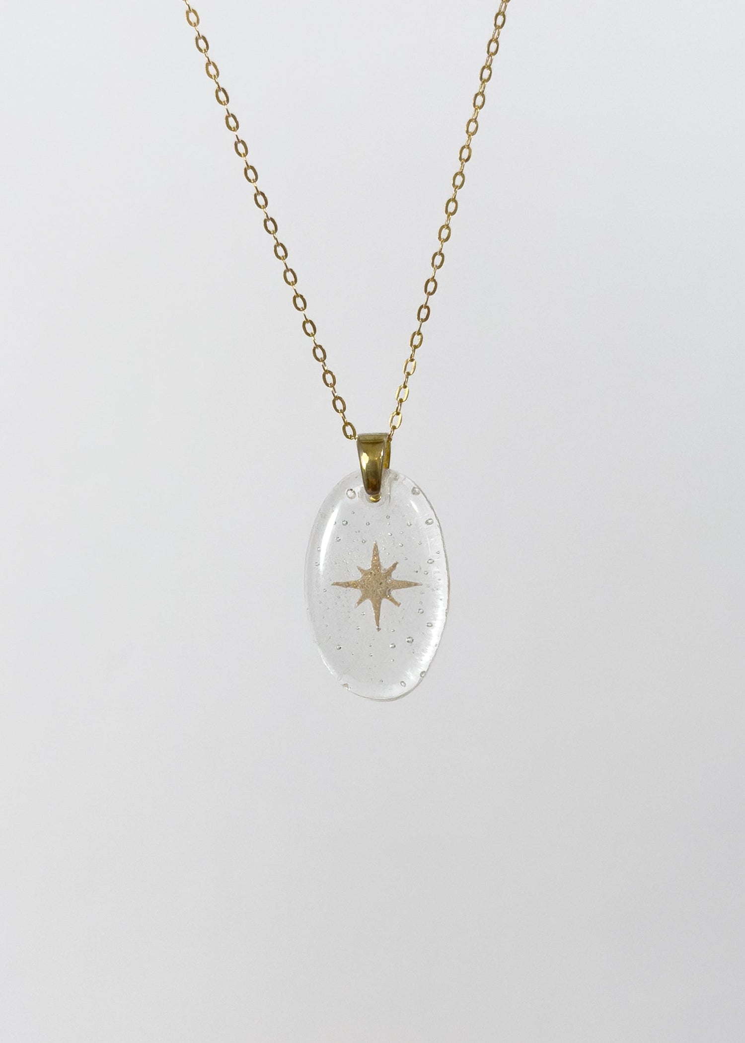 Clear glass pendant necklace with gold star design made out of cremains on a white background