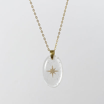 Clear glass pendant necklace with gold star design made out of cremains on a white background