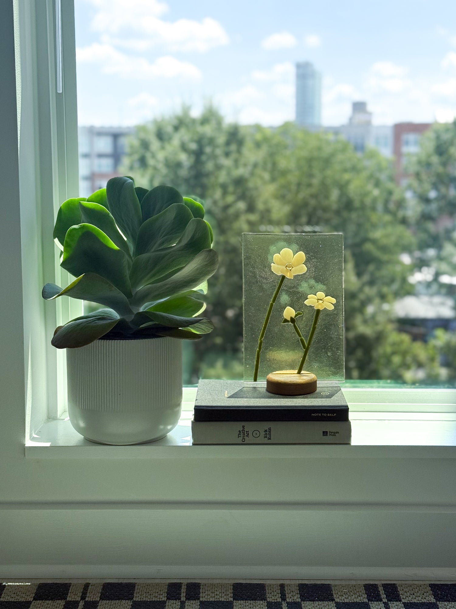 A glass memorial suncatcher with the ashes and cremains embedded into the pistol of the flower sitting on a wood stand in a widow with the light pouring through it