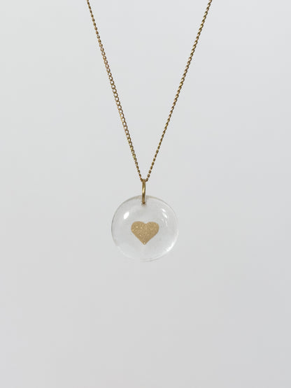 Clear glass pendant necklace with a gold heart design made out of cremains and ashes on a white background