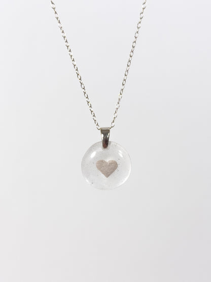 Clear glass pendant necklace with a silver heart design made out of cremains and ashes on a white background
